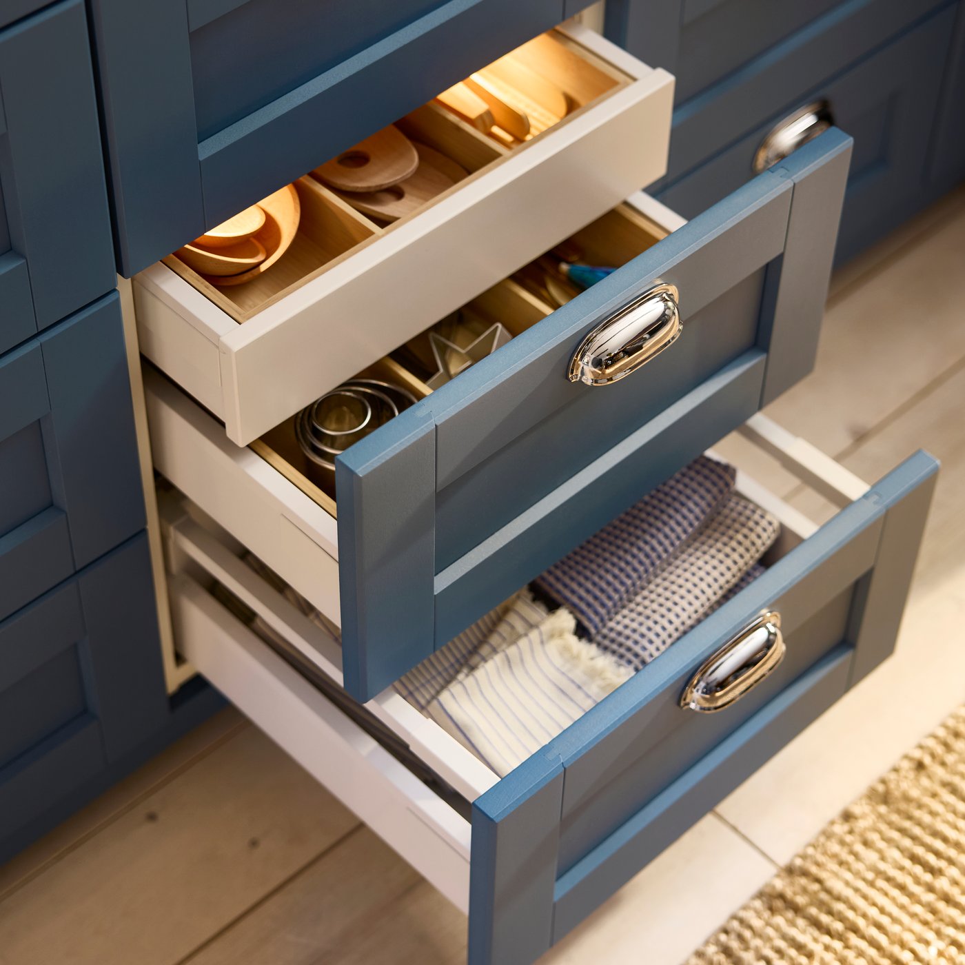 Due cassetti in un'isola cucina con frontali blu LERHYTTAN sono stati aperti. Uno di essi ha un cassetto nascosto all'interno.