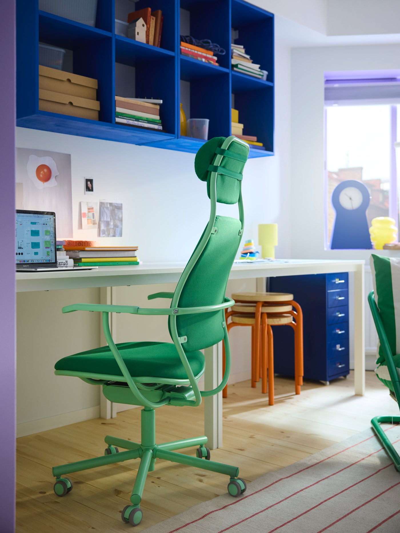 A bright green LÖPARBANA gaming chair by a desk with blue shelves on the wall behind it. Blue and orange details in back.