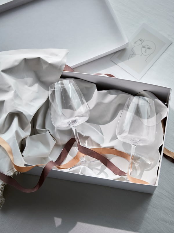 Two DYRGRIP wine glasses lying in a paper box with lots of paper wrapping and coloured string giving an elegant impression.