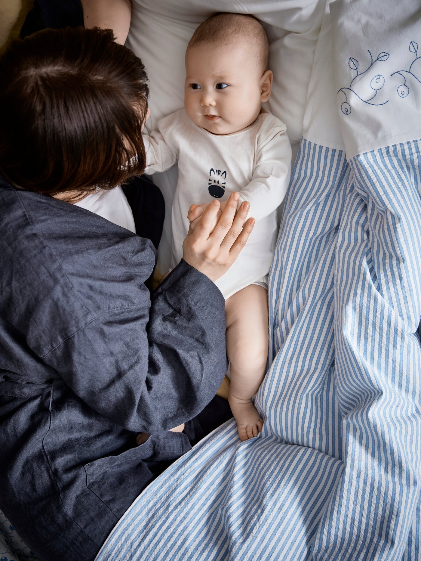 Prikaz popluna i jastuka unutar KLÄMMIG crveno-tirkizne navlake za poplun i jastučnice za krevetić na drvenom stolcu.