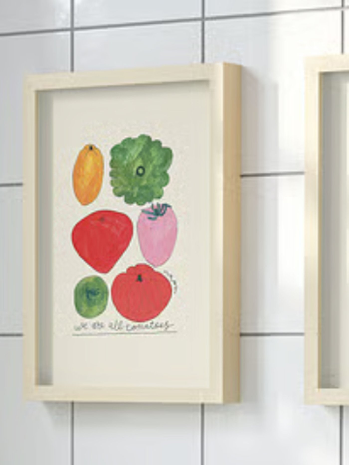 Tavla med målade grönsaker i fururam upphängs på vit kalelvägg. 