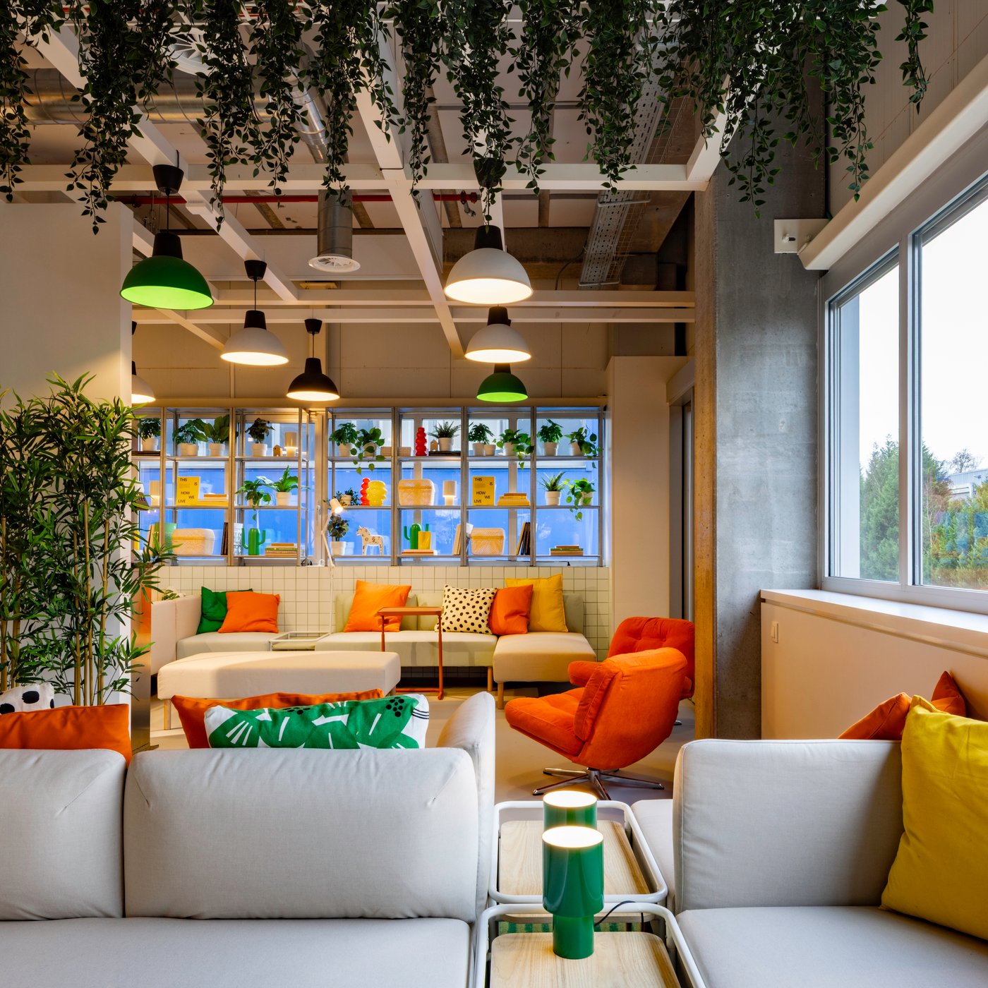 Un espace ouvert et coloré, avec du mobilier IKEA confortable, de vives touches d’orange et beaucoup de verdure, crée un endroit accueillant pour faire une pause ou se retrouver de manière informelle.