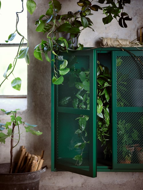 Salon avec armoire verte à portes en acier et tablettes réglables placée à côté d’une fenêtre.