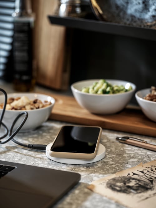 Prim-plan în bucătărie al unui încărcător wireless alb minimalist în fața unei tăvi bej cu 3 boluri albe.