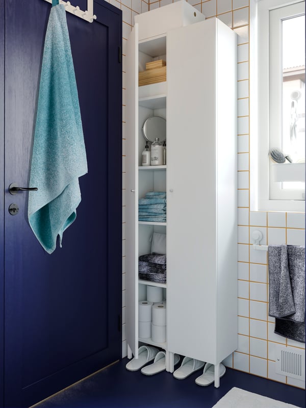 NYSJÖN high cabinet next to the shower in a small bathroom with white tiles.