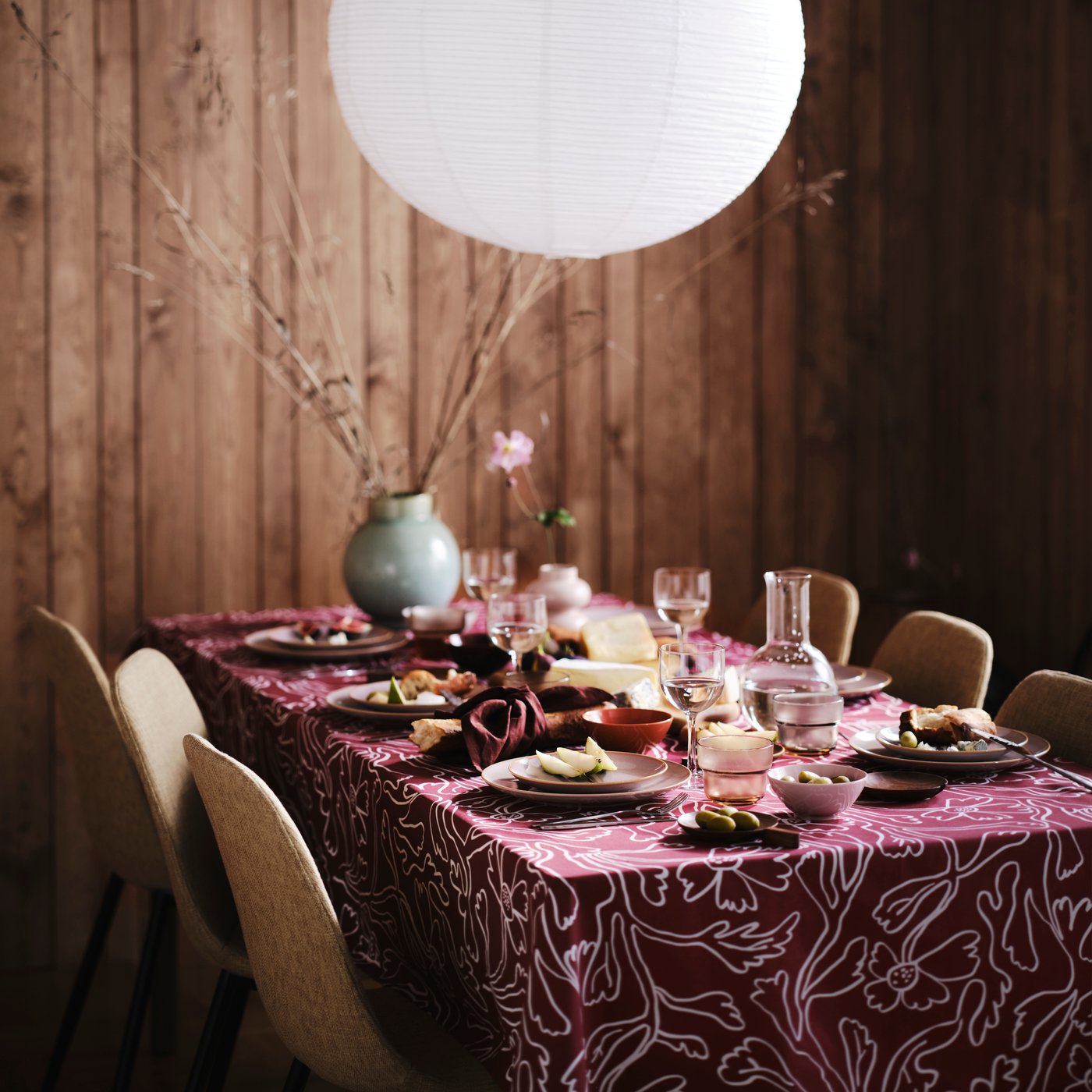 A table set with cheese and wine on a patterned tablecloth with mouth-blown STOCKHOLM wine glasses and FÄRGKLAR plates.