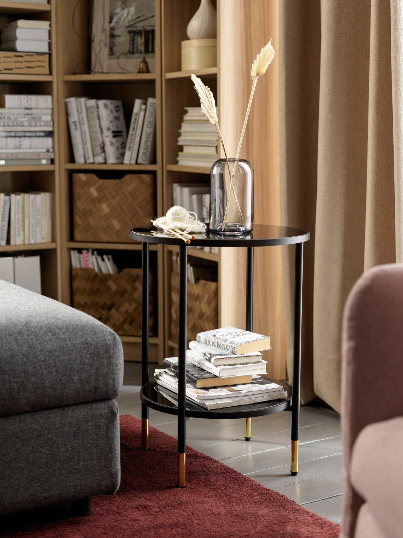 Salón moderno con una mesa auxiliar redonda, una alfombra rectangular de pelo corto, un jarrón, una caja rectangular y una librería.
