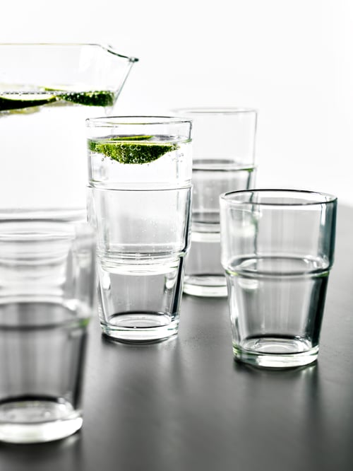 Drinking glasses placed on a black countertop beside a water jug with lime slices.