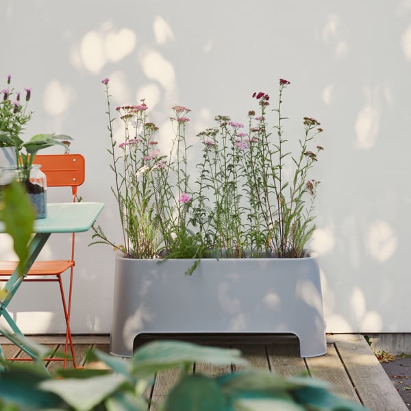 A patio setting with an orange chair beside a grey ASPAREN planter filled with flowers, adding colour to the outdoor space.