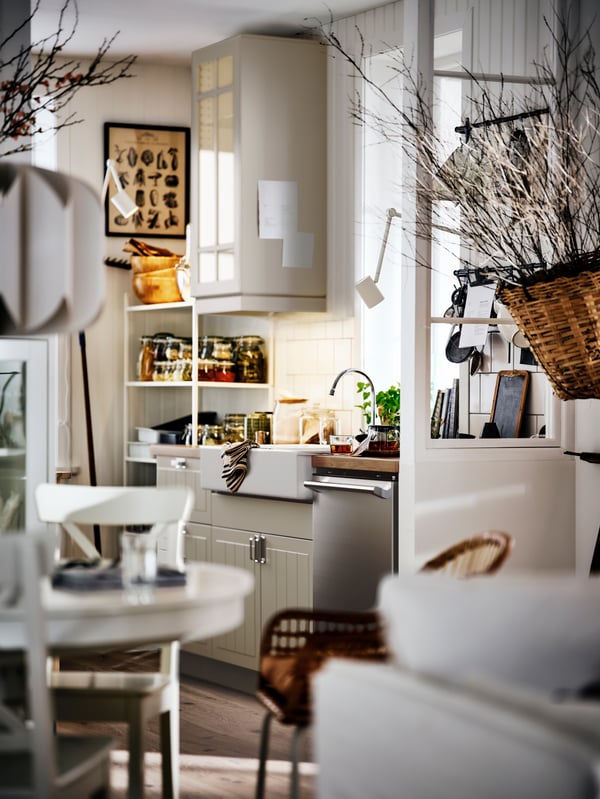 A bright, beige country-style kitchen and dining area, with white cabinets, a round table and decorative dried branches.