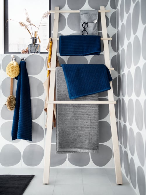 Modern bathroom with ladder-style towel stand with bath towels hanging, white and grey tiles and bath rug.