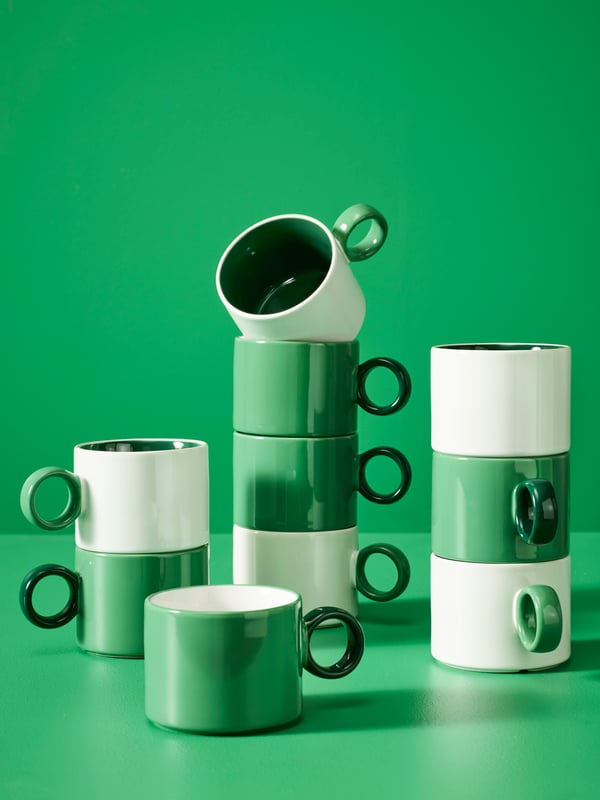 White and green PIGGÅL mugs stacked on top of each other in a space with green walls and floors.