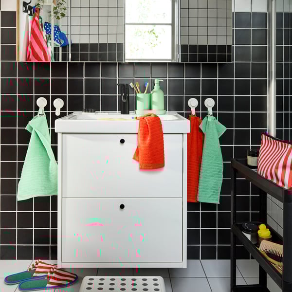 A white HAVBÄCK/ORRSJÖN wash-basin with two drawers and four mirrored cabinets above. Colourful towels on white hooks.