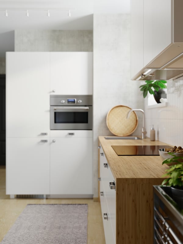 Vue latérale d’un plan de travail sur mesure HOLMARED en placage de bambou encadrant des meubles blancs dans une cuisine en L aérée et lumineuse.