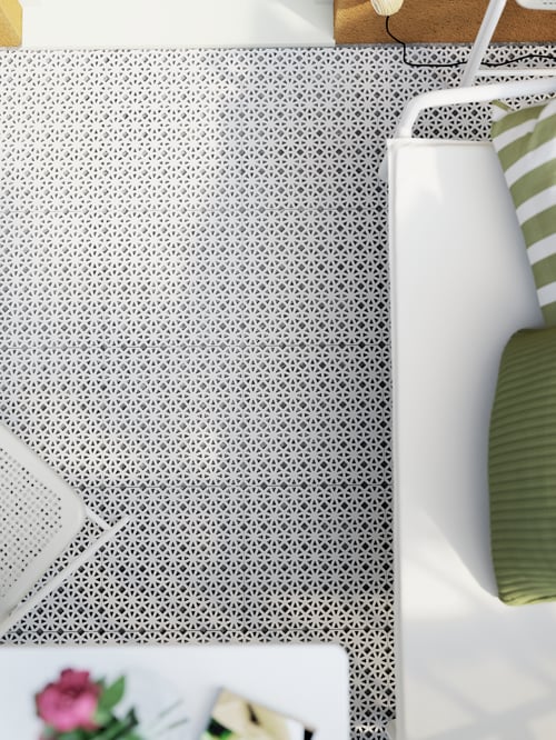 An overhead shot of a grey floor decking on which is an outdoor two-seat sofa with cushions, a balcony table and a chair.