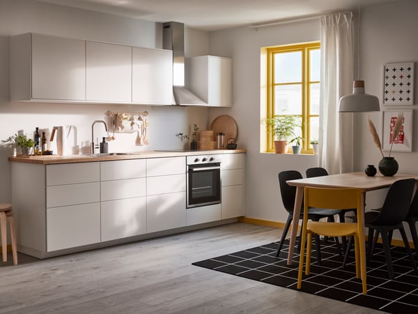 Man sieht eine minimalistische Küche mit matten, grifflosen Fronten und einer Arbeitsplatte aus Holz. Vor der Küche steht auch ein LISABO Esstisch mit vier Esszimmerstühlen.