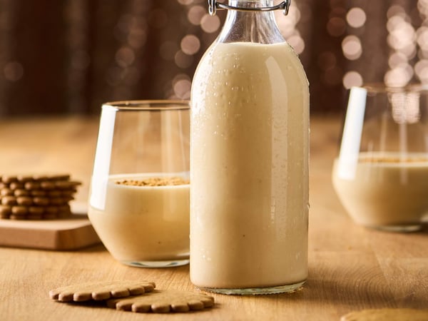 Creamy coquito in a glass bottle on a wooden table, with two filled glasses and cookies arranged around it.