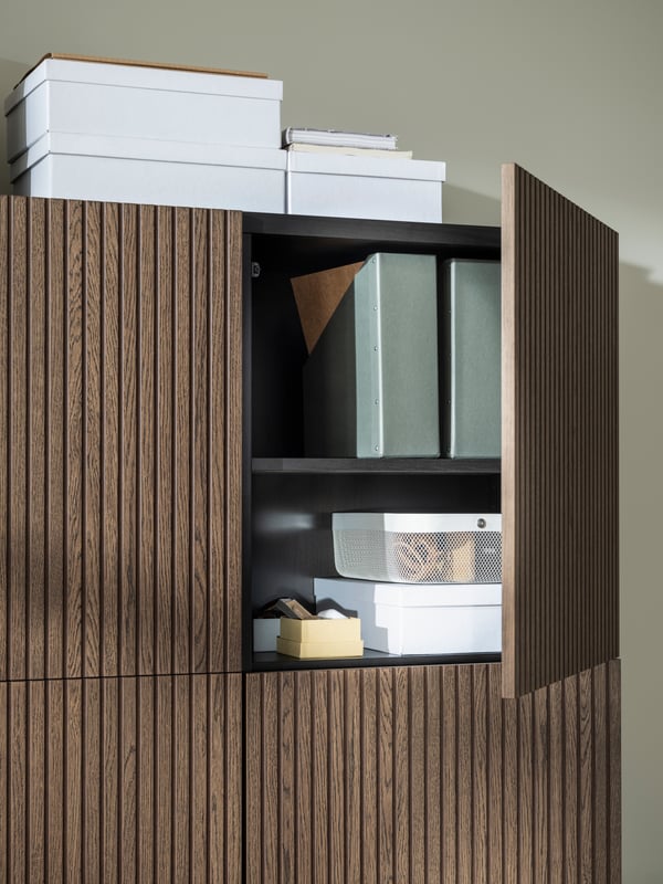 White TJENA storage boxes in and on top of black-brown BESTÅ cabinets with brown-stained oak-veneer BJÖRKÖVIKEN doors.