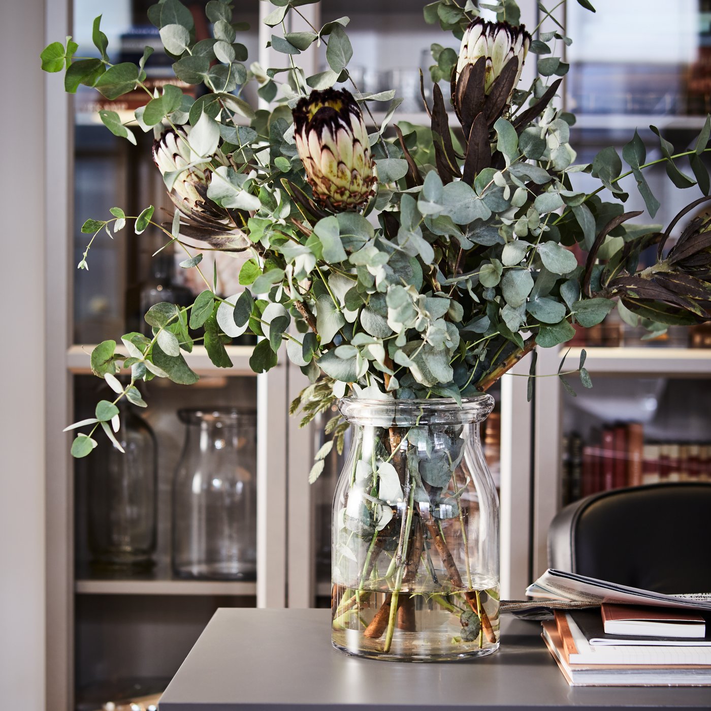 مزهرية من الزهور فوق سطح رمادي ومكتبات BILLY في الخلفية.