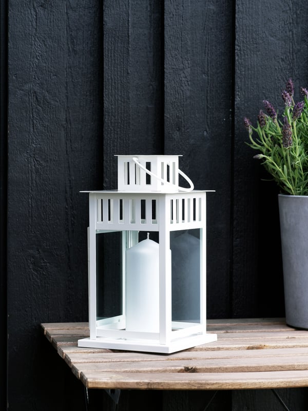 A white BORRBY lantern with a lit candle inside is sitting outdoors 