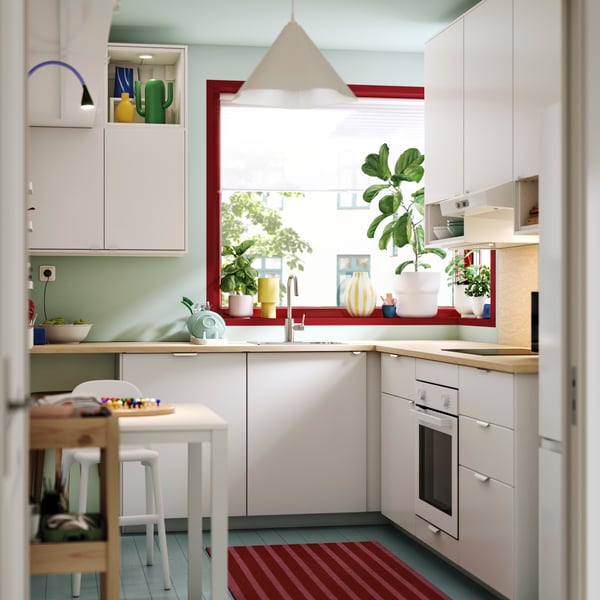 Una cucina luminosa con ante VEDDINGE bianche, pareti verde chiaro e piante sul davanzale.