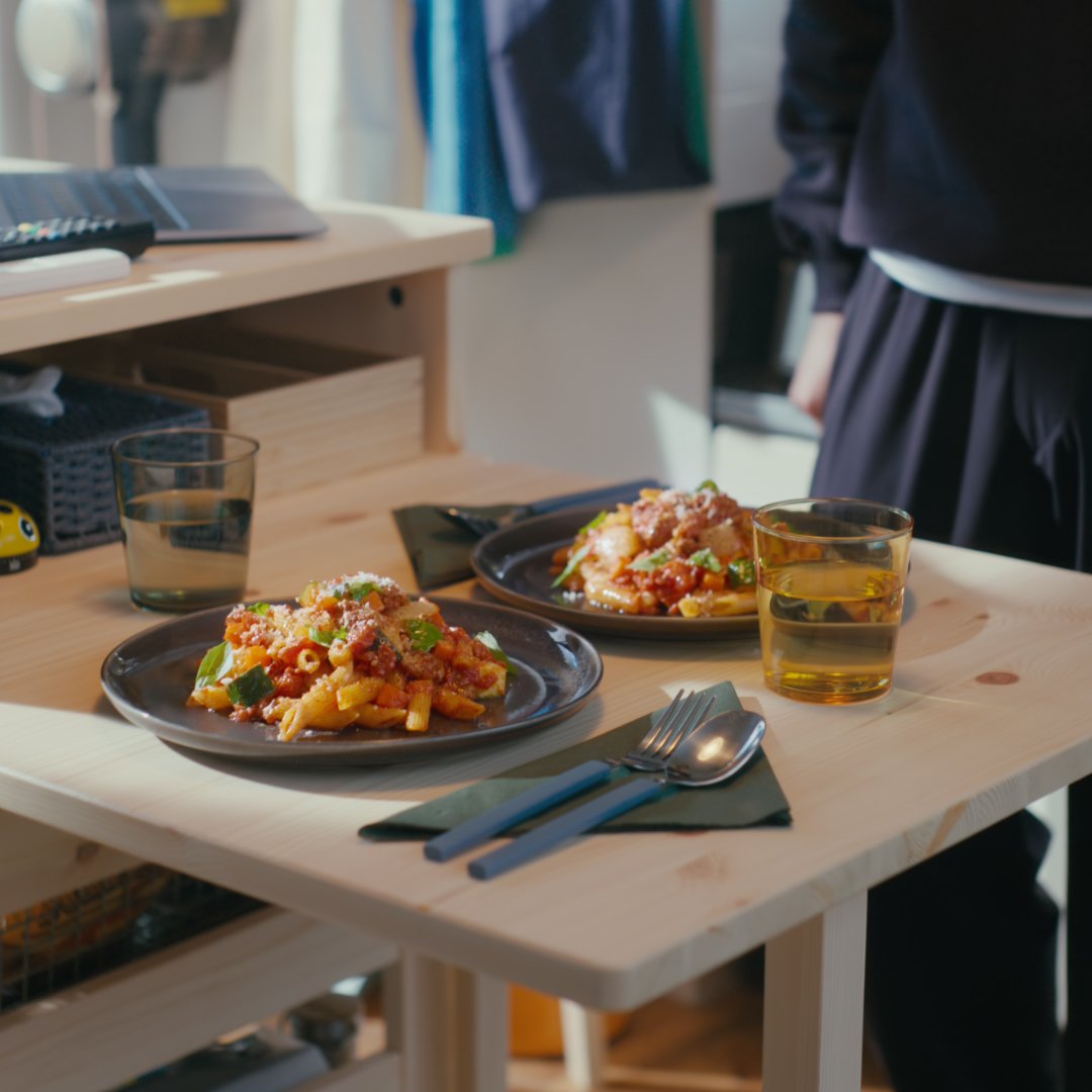 Casual dining table with pasta dishes and glasses on wooden surface
