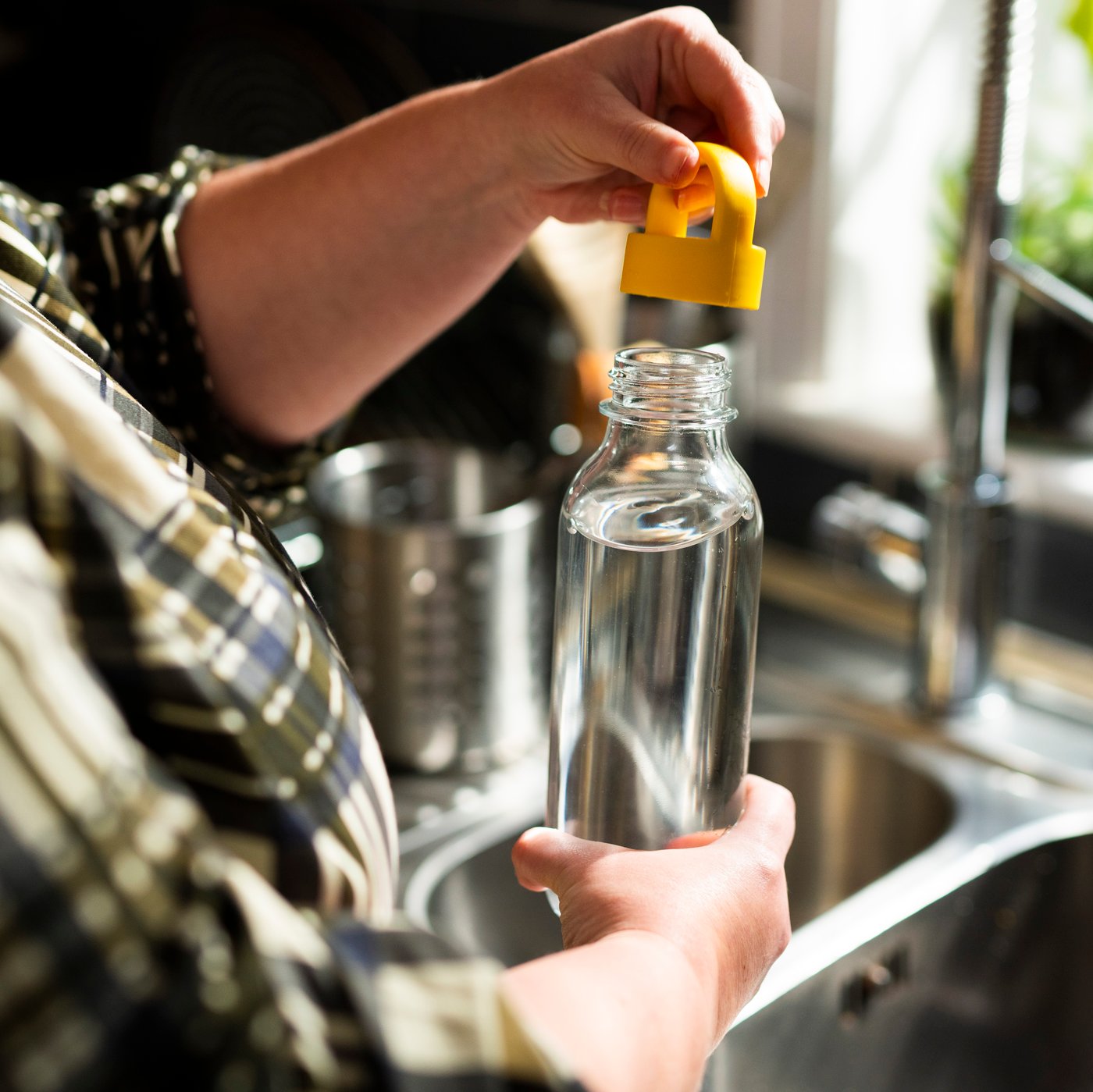 A woman in a kitchen is filling a FORMSKÖN water bottle with water.