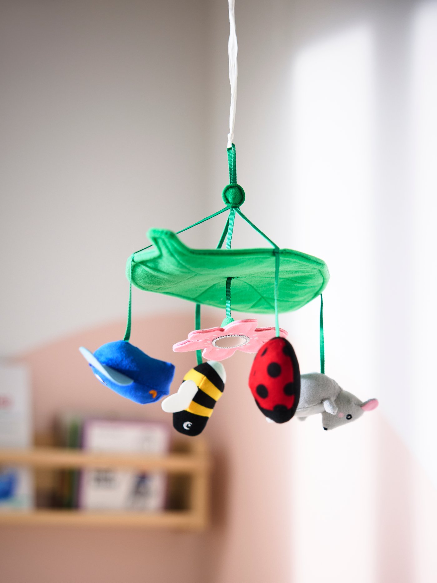 Närbild av SANDBI mobil med en grön bladform och hängande figurer: en blomma, ett bi, en nyckelpiga, en mus och en fågel i olika färger.