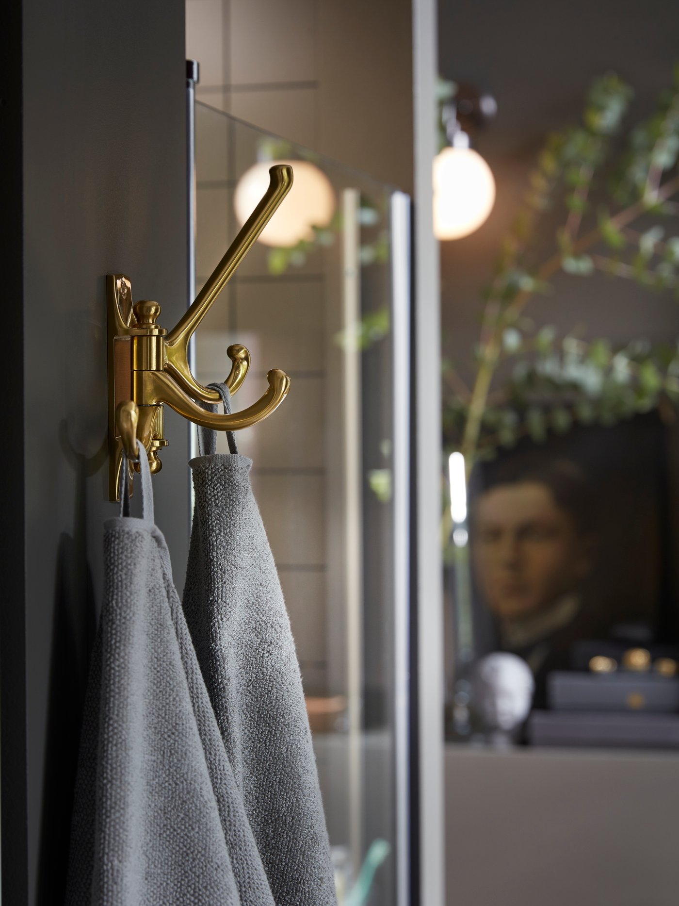 KÄMPIG 3-armed swivel hook in brass-colour is mounted on a wall next to a shower, two grey towels hang from the hooks.