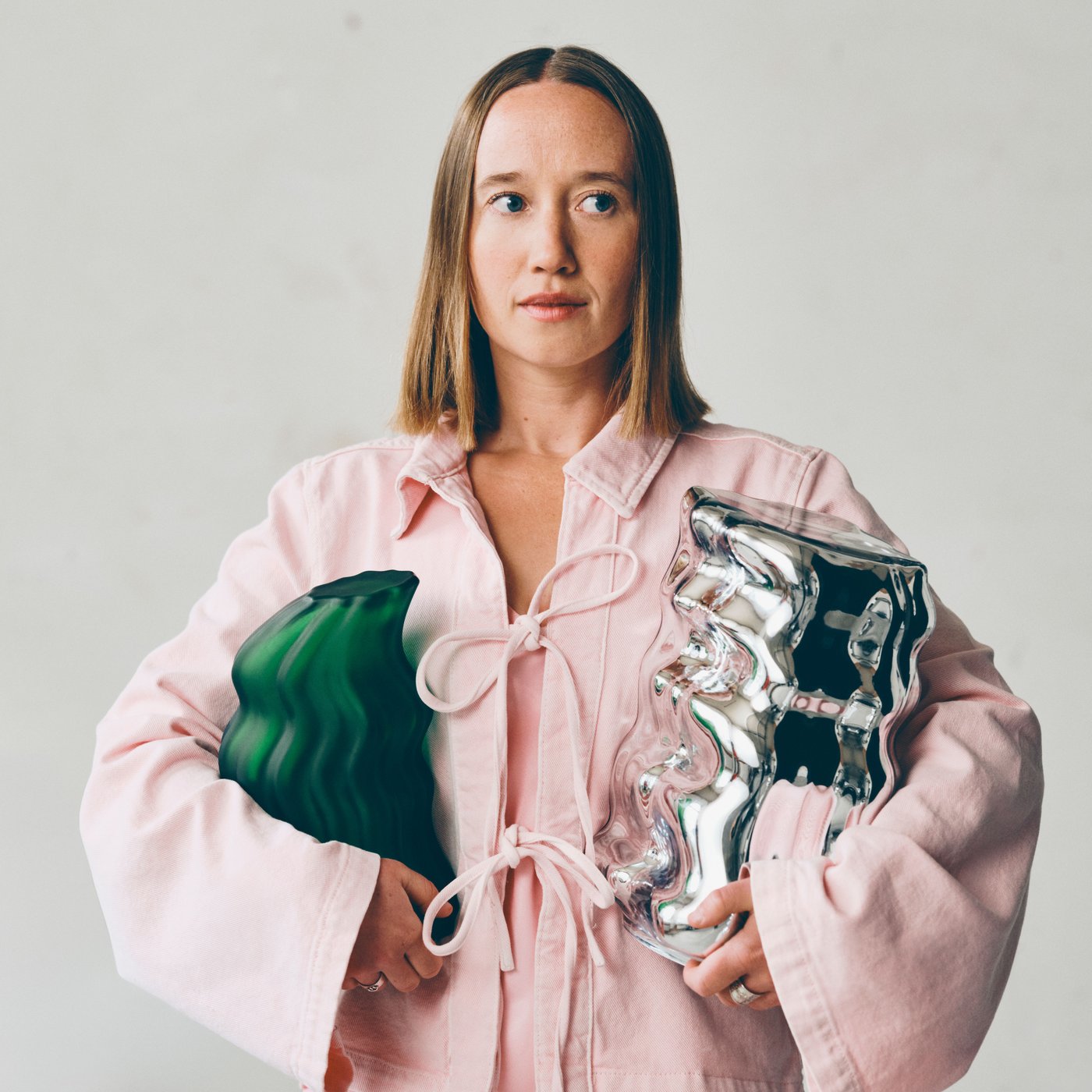 Close up of Lisa Resier in a pink dress holding a green and a metallic sculpture made for IKEA art collection KONSTRUNDA.
