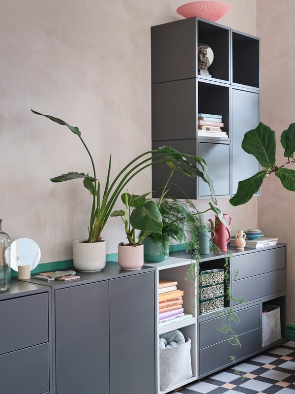 A cabinet combination in gray and white with shelves, drawers and doors. Green plants, books and decorative items stand here.