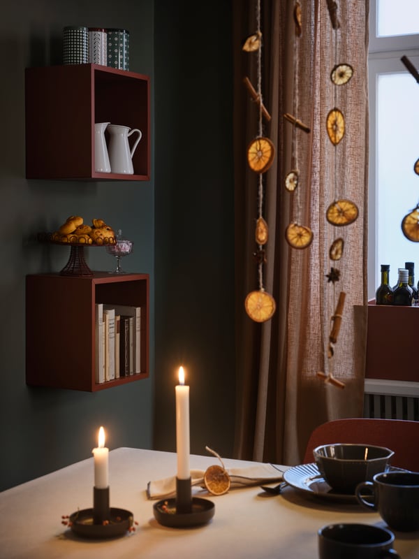 A dining room with lit candles and a dried orange garland hanging from the ceiling. 