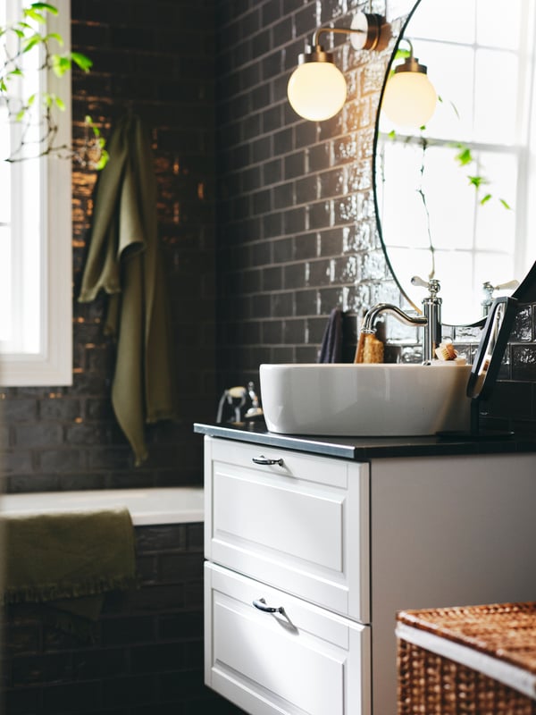A light green VALLASÅN bath towel on a hook near a white GODMORGON wash-stand with 2 drawers below a LINDBYN mirror.