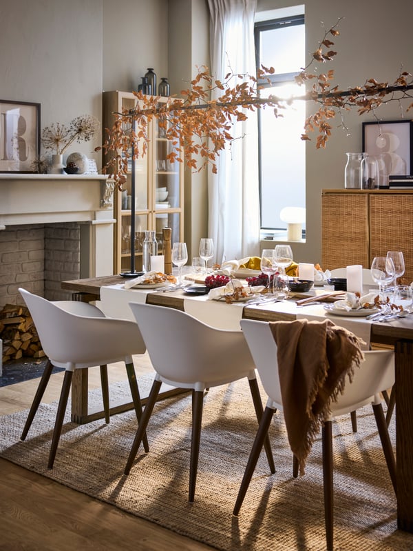 A table set in autumn style with white table runners, white GRÖNSTA tub chairs, and a LOHALS rug on the floor.