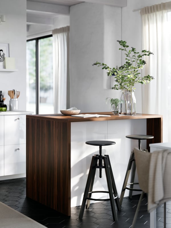 A white kitchen island with a worktop and cover panels in a dark walnut effect is placed in a kitchen with RINGHULT fronts.