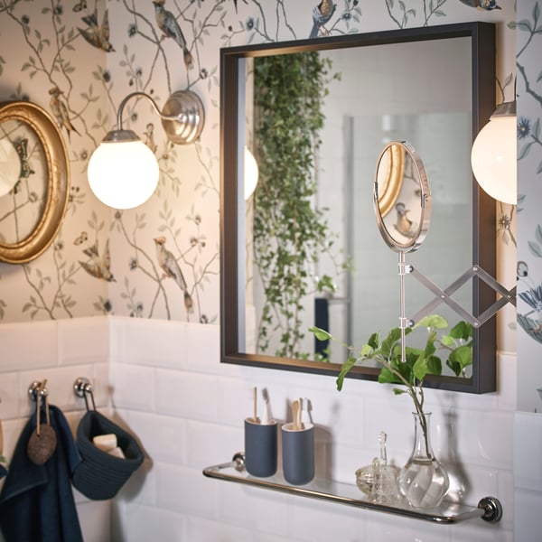 A NISSEDAL mirror with a black frame and  stainless steel FRÄCK mirror is in a bathroom.