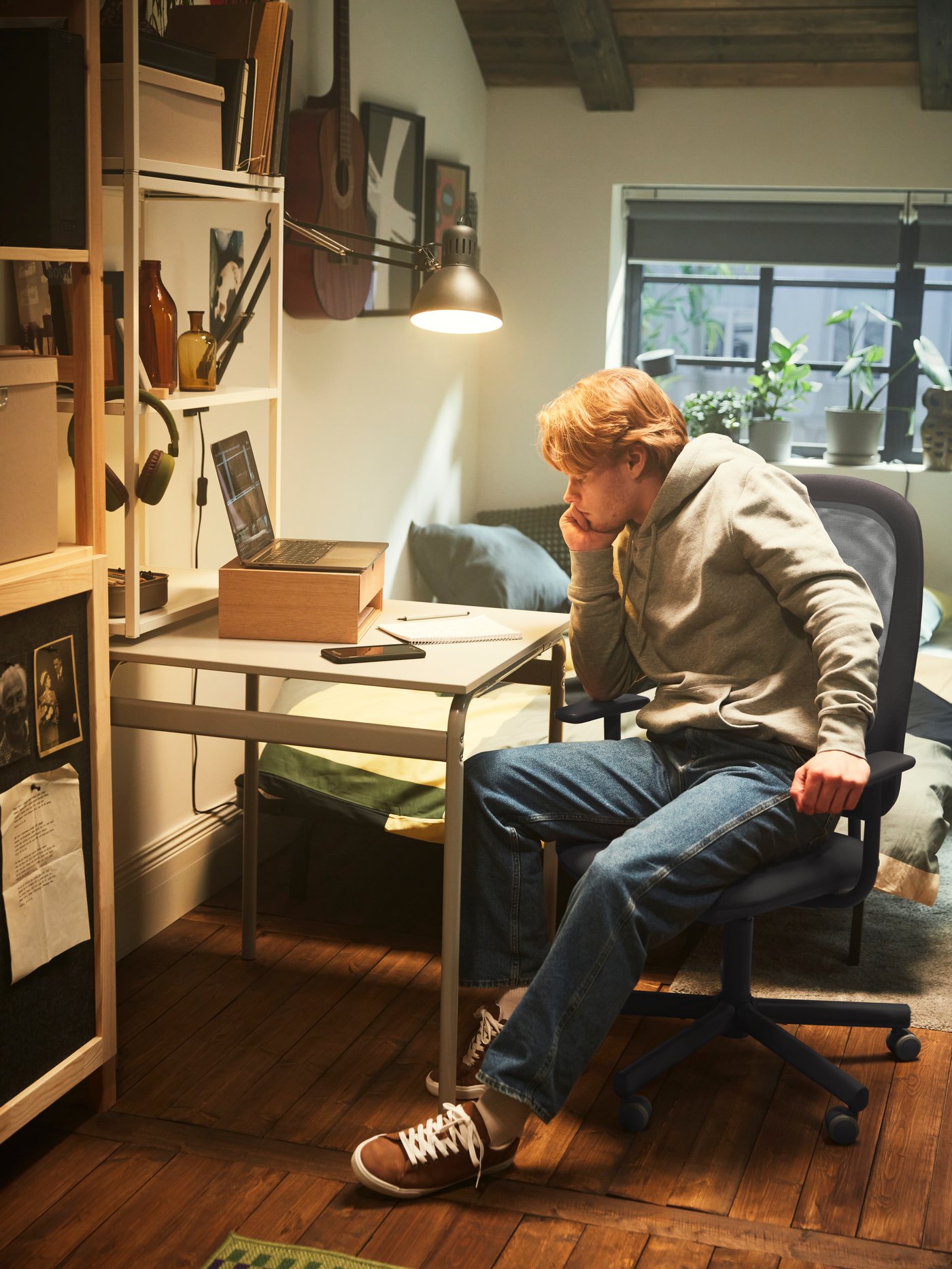 Garçon assis à son bureau et regardant un cahier, un ordinateur ouvert dans sa chambre d’étudiant.