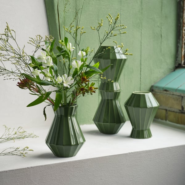 Four MÄVINN vases in green stoneware stand on a white ledge. One has flowers in it and two are piled on top of each other.