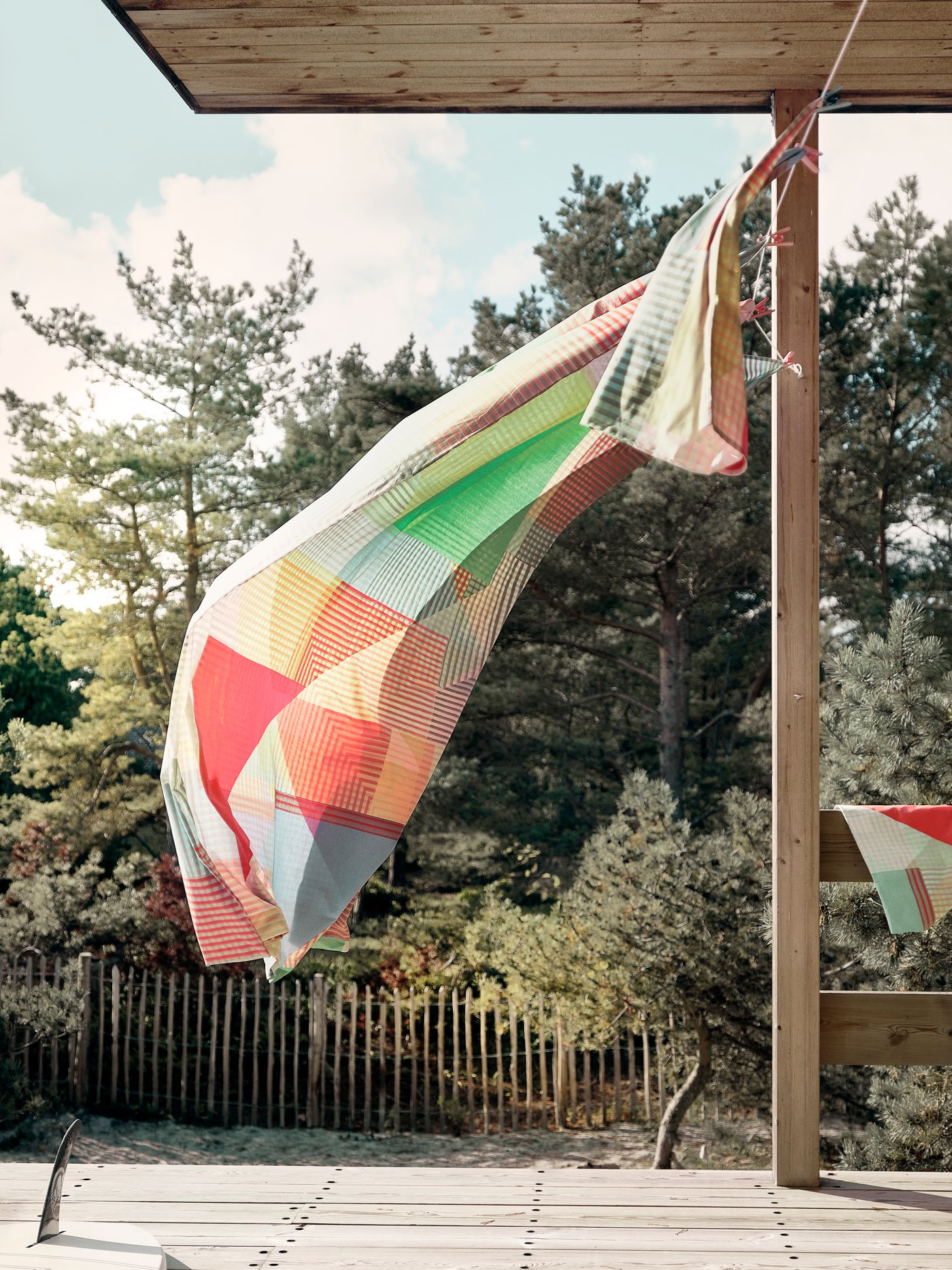 Hanging from a clothes line on a wooden patio, the PIMPERNÖT quilt cover and pillowcase blow gently in a summer breeze.