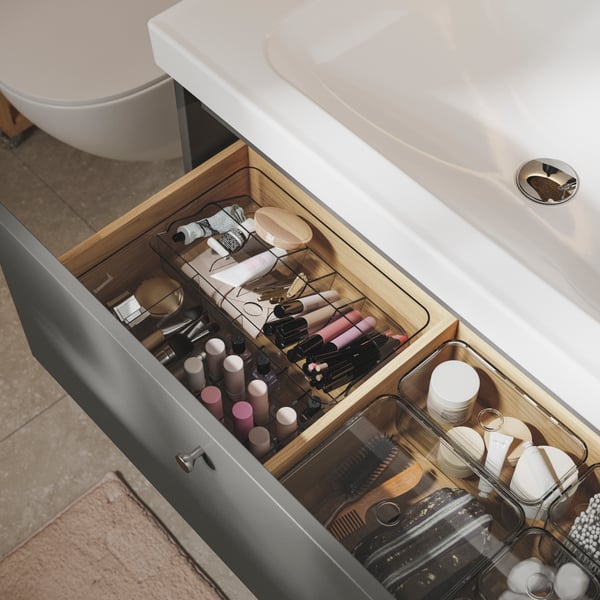 Das Innere einer HAVBÄCK Waschtischschublade, organisiert mit kleinen transparenten Boxen, die mit Make-up, Werkzeugen und Accessoires gefüllt sind.