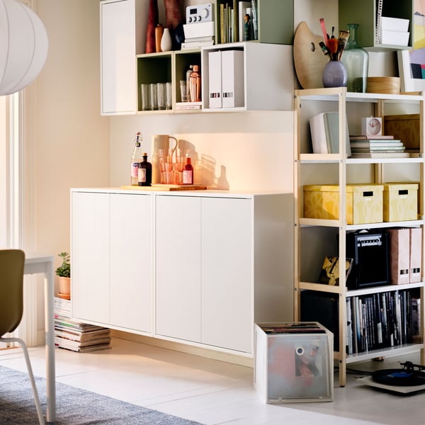 An out corner in a light living room around which a combo of EKENABBEN open shelving units and EKET cabinets are arranged.