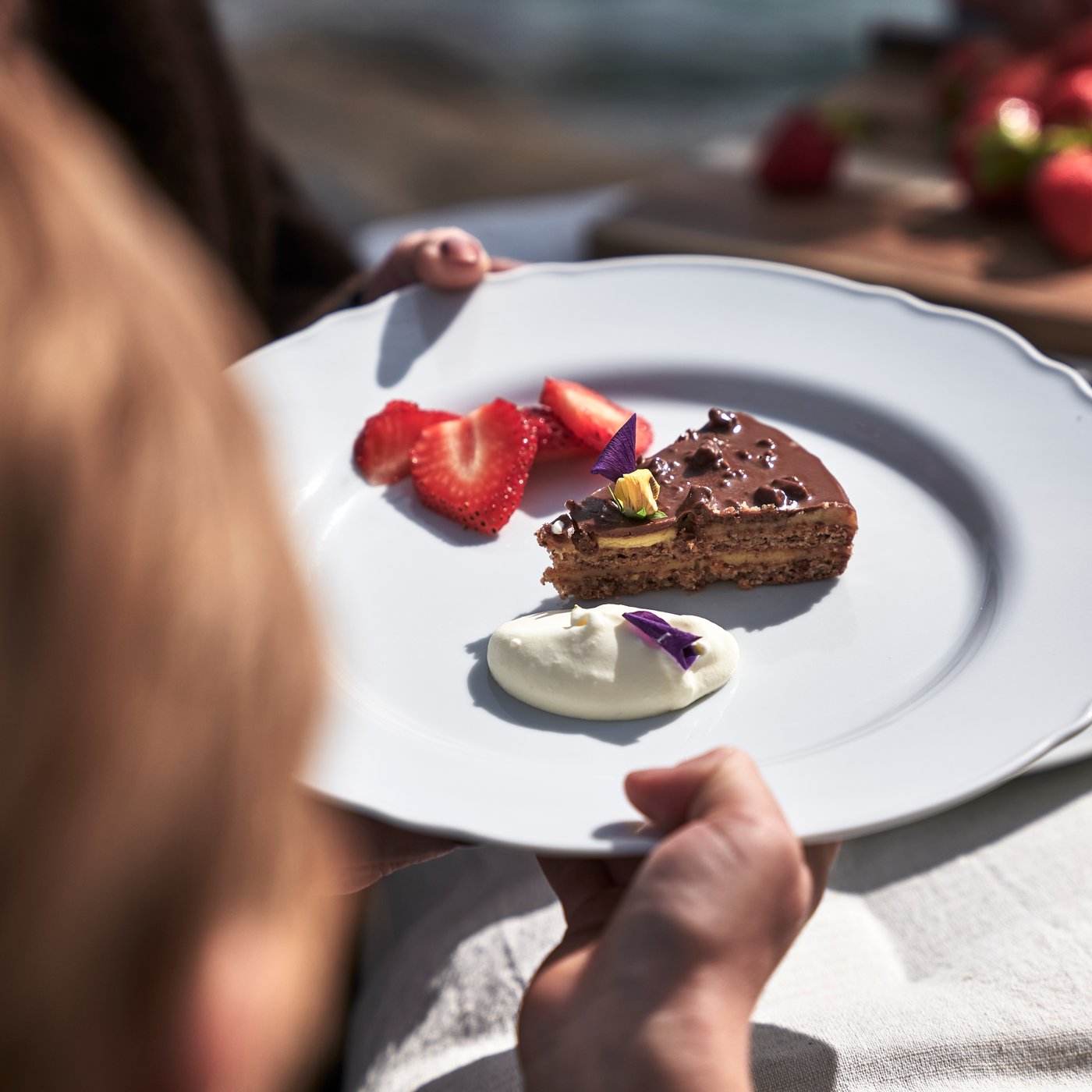 A plate with sliced ​​strawberries, a slice of Daim cake, and whipped cream.