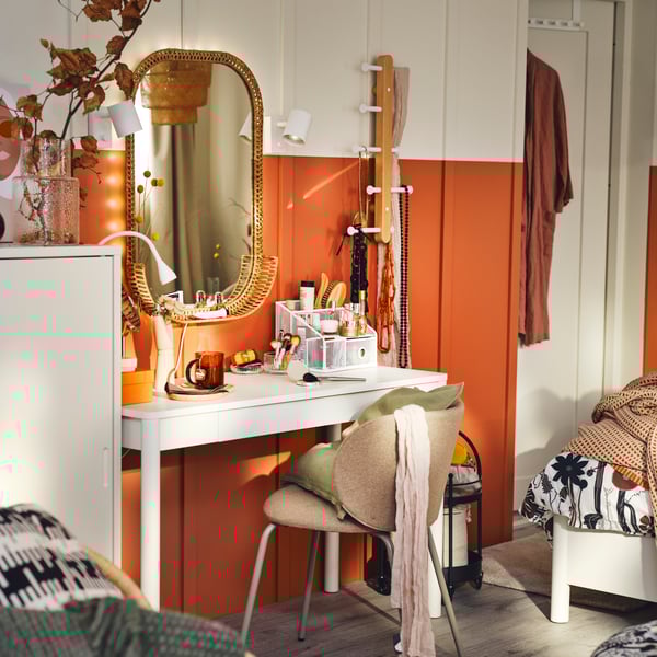 A white DRÖNJÖNS desk and a beige KRYLBO chair in front of a rust coloured wall with a SOMMARBO rattan mirror on it.