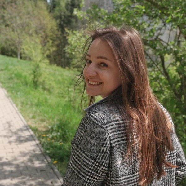 Nataliia, smiling brightly, walks along a picturesque path surrounded by lush greenery.
