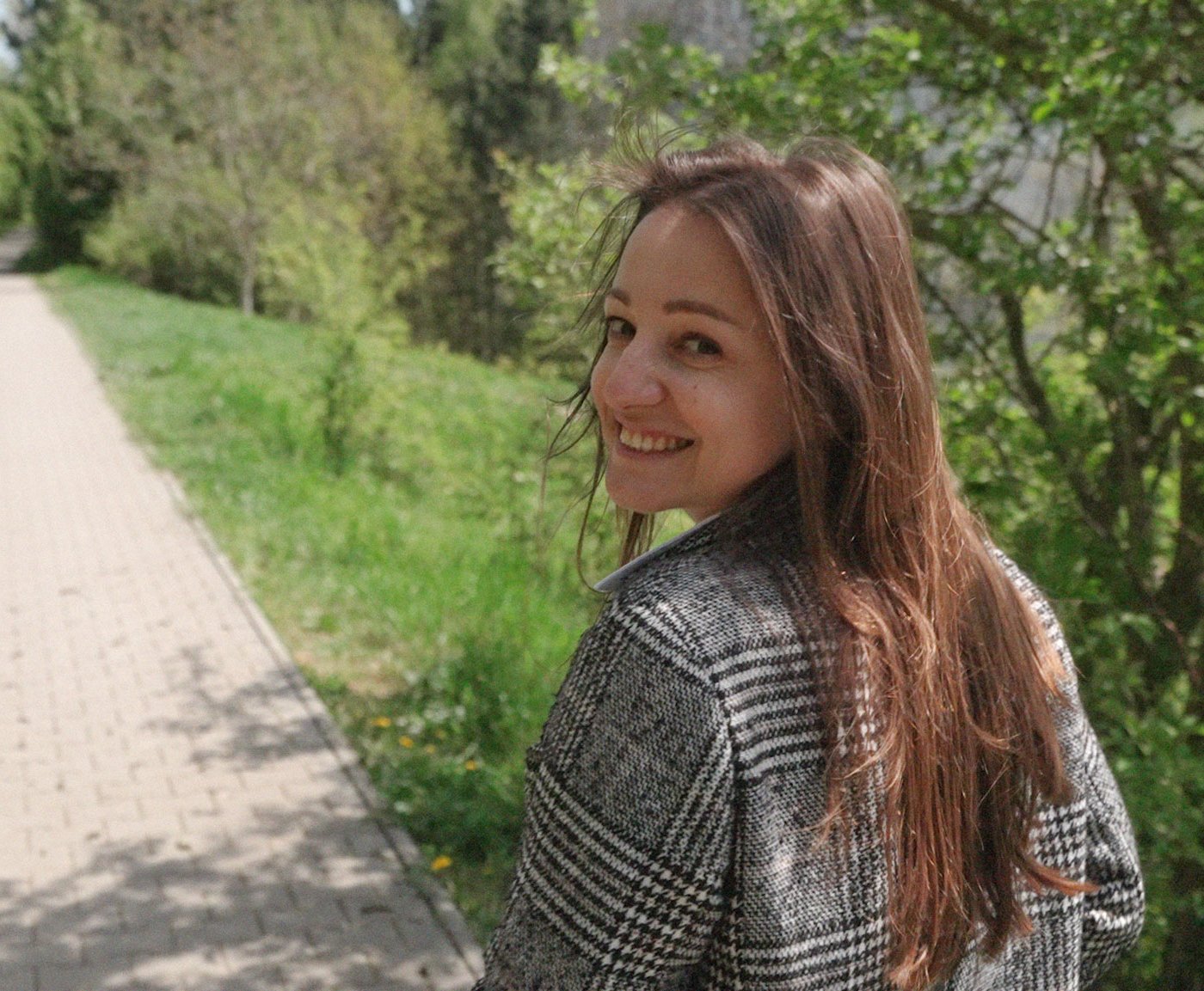 Nataliia geht mit einem strahlenden Lächeln einen malerischen Weg entlang, der von üppigem Grün umgeben ist.