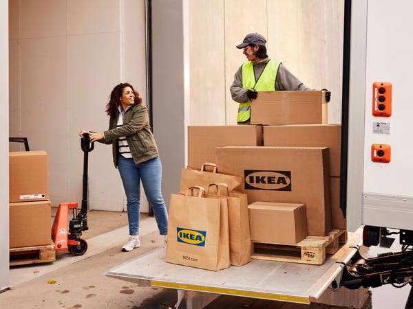 En leende kund håller i en pallbock med stora IKEA-paket och pratar med en drivare som har fler paket att lasta av.