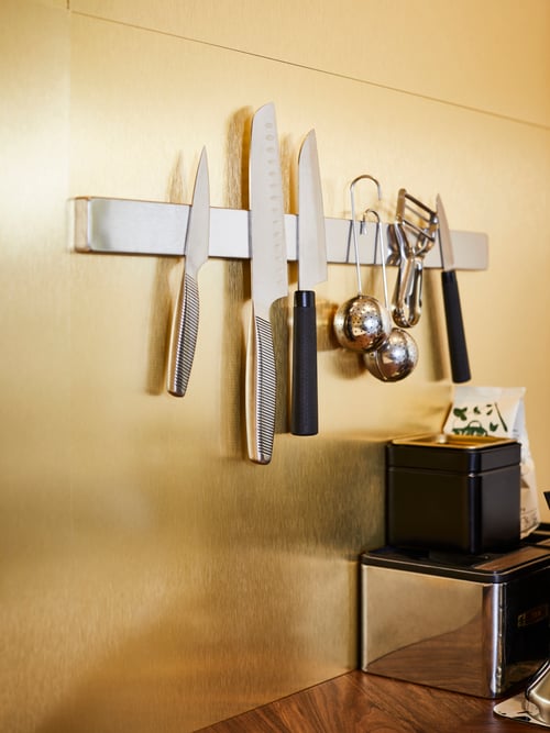 Kitchen with magnetic rack on wall, vegetable knife, paring knife, tea infusers, vegetable peeler, tin with lid, coffee.