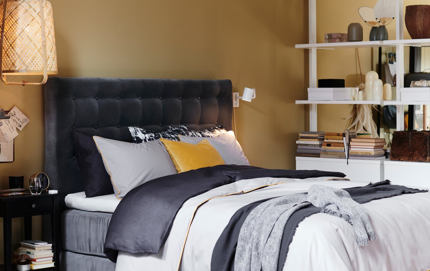 Ein Bett mit einem grau gesteppten Kopfteil und Bettwäsche in verschiedenen Schichten