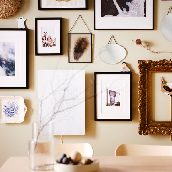 A picture wall over an ash RÖNNINGE table, with black RIBBA and LOMVIKEN frames plus other frames and decorative items.