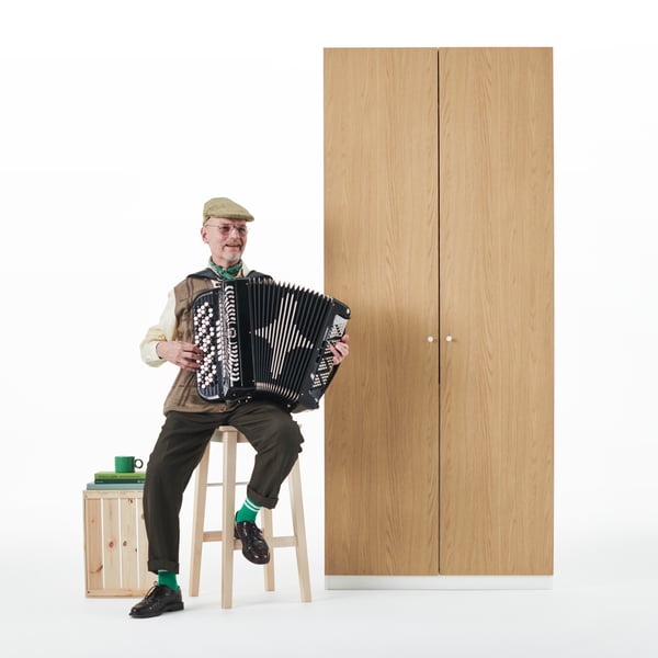Un uomo che suona la fisarmonica è seduto su uno sgabello IKEA accanto a un guardaroba PAX.